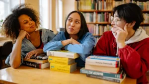 Tre studenti universitari studiano insieme in biblioteca tra i libri