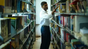 Uno studente cerca un libro tra gli scaffali di una biblioteca universitaria